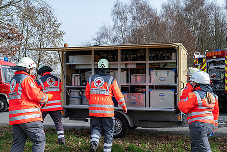 Notarztübung 2026 Das Bild zeigt einen Transportwagen des DRK umgeben von Natur. Die Einsatzkräfte tragen Einsatzkleidung und sind mit der Entladung der Materialien beschäftigt. Das heißt, sie laden Verbandsmaterial aus dem Fahrzeug.