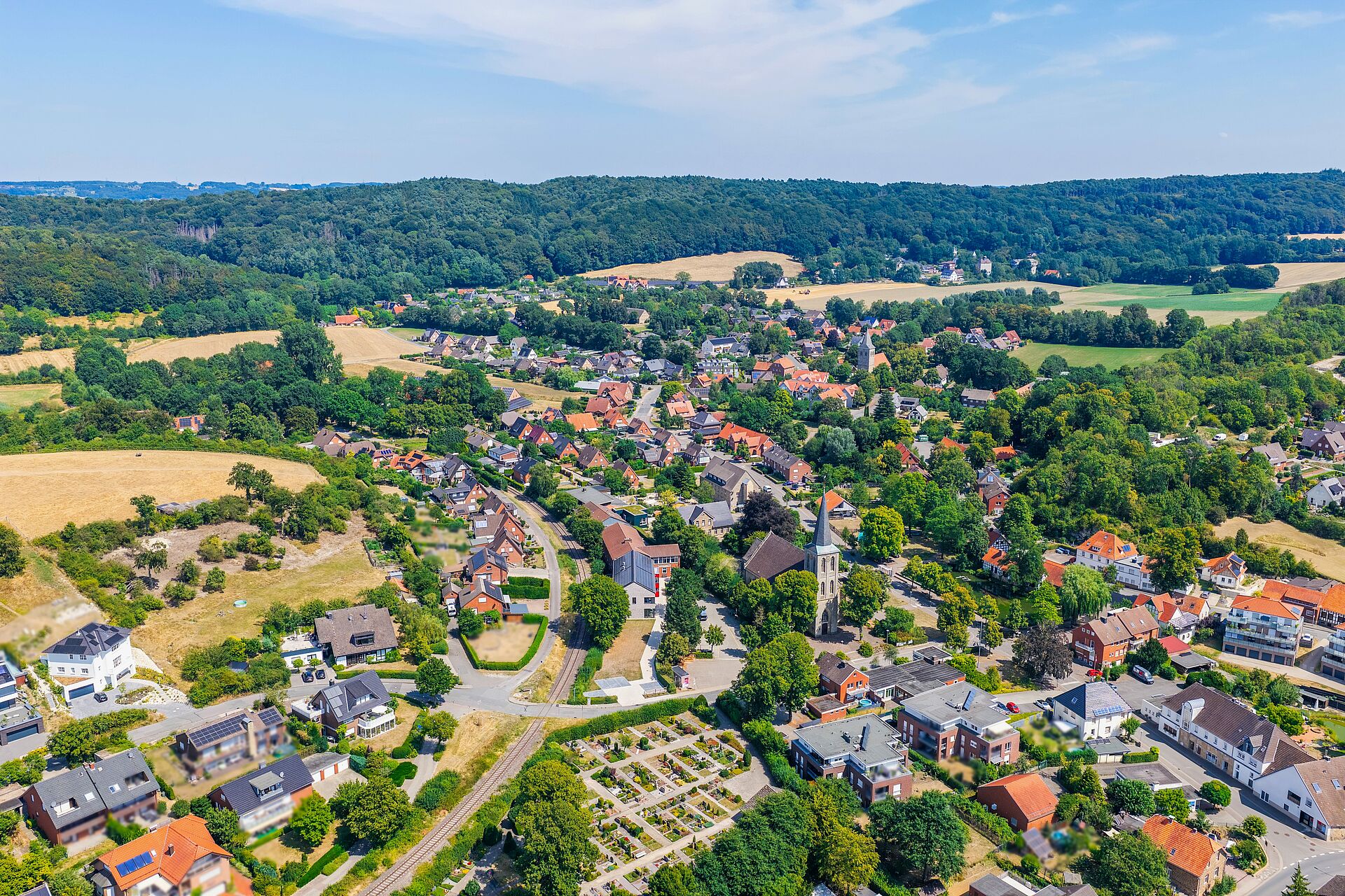 Brochterbeck im Tecklenburger Land Luftaufnahme des Ortes Brochterbeck: Das Dorf mit seinen rot gedeckten Häusern liegt eingebettet in grüne Felder und Wälder; im Zentrum hebt sich die Kirche mit ihrem hohen Turm ab, im Hintergrund bewaldete Hügel.